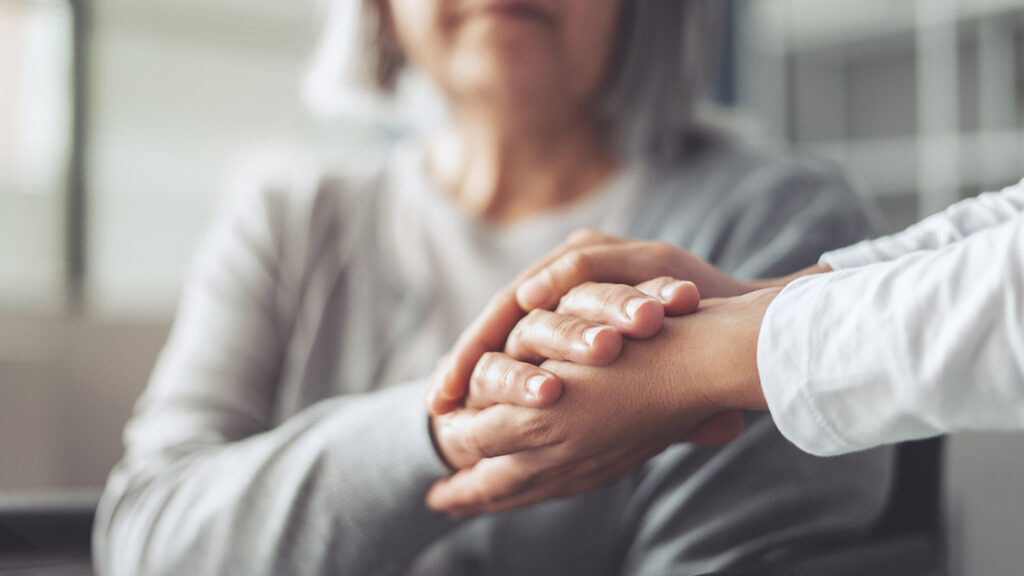 Close-up of an older woman being comforted as a younger person's hand gently rests on hers, expressing support and compassion.