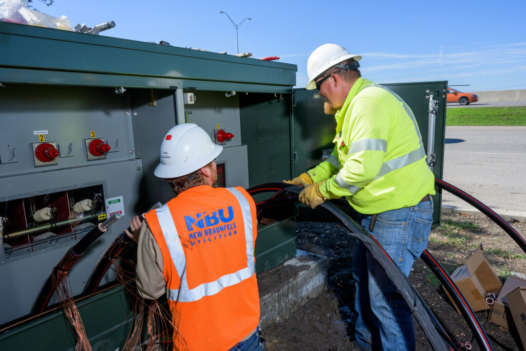 Electric crew members working on a transformer in shopping area.