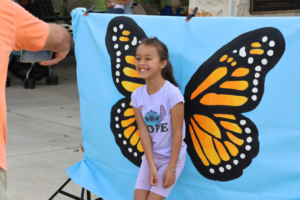 Young girl in purple shirt poses for a photo in front of a butterfly painting