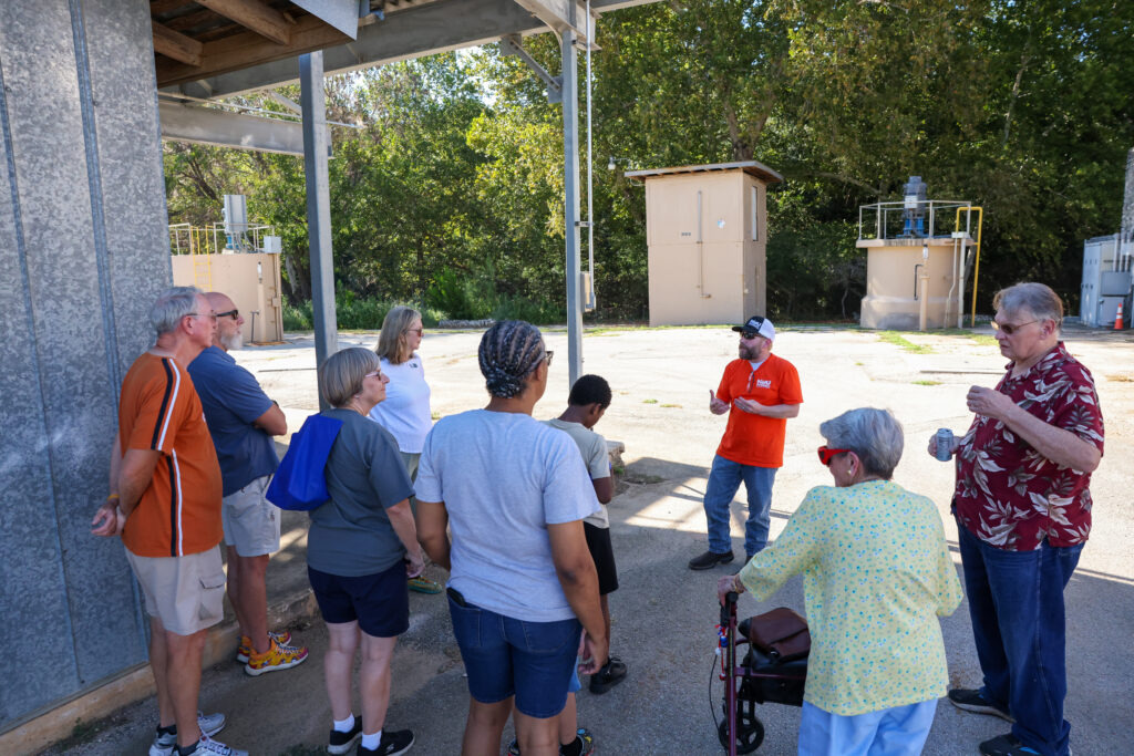 NBU employee stand with children and their families as he gives a tour of the well yard at Headwaters