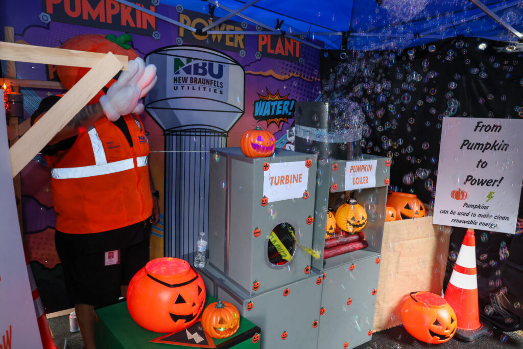 Inside the spooky house at NBU's Spooktacular. Orange pumpkins, safety cone, and equiptment fill the space with NBU background of water tower.